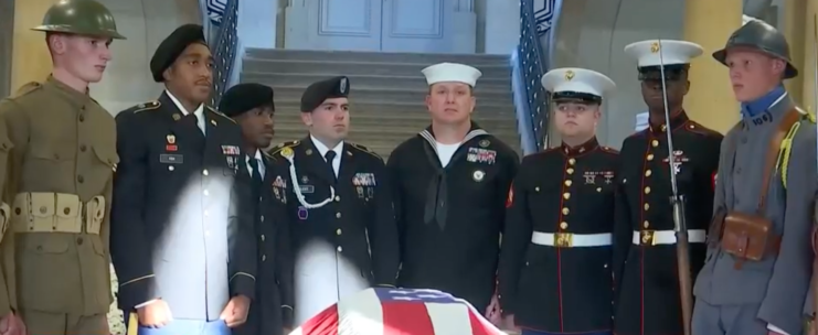 French and US soldiers gathered around an American flag-draped casket