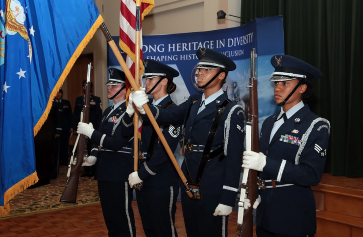 Four female members of the Honor Guard standing with flags and their rifles