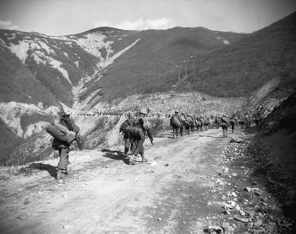 11/15/1950-North Korea- U.S. Marines slog up a mountain road in their advance to the Changin (Chosin) Reservoir, big source of electric power for North Korea. On the hillside may be seen three power transmission towers. This is the type of country made for guerrilla, hit-and-run tactics, where a few machine guns on the ridges could do devestating damage to troops using the lwo road. (Photo Credit: Bettmann / Getty Images)
