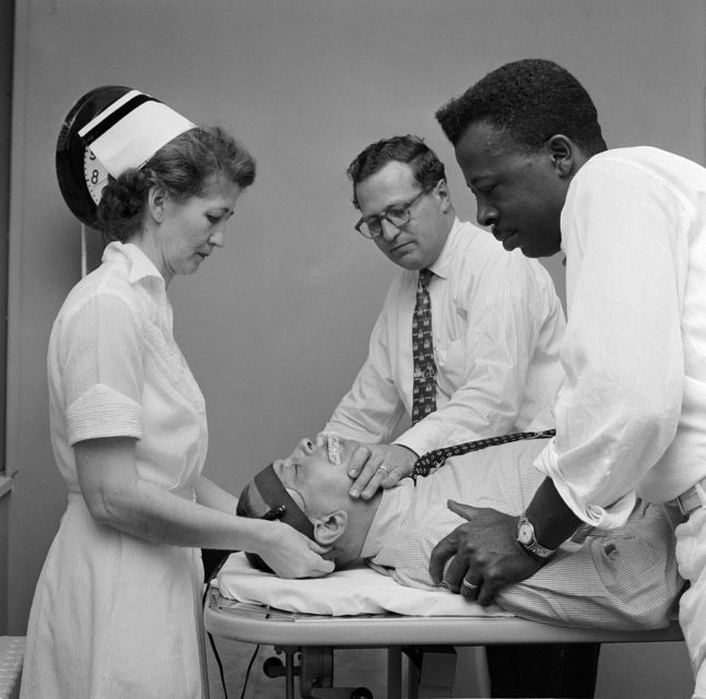 Two doctors and a nurse standing over a man who is lying on a gurney