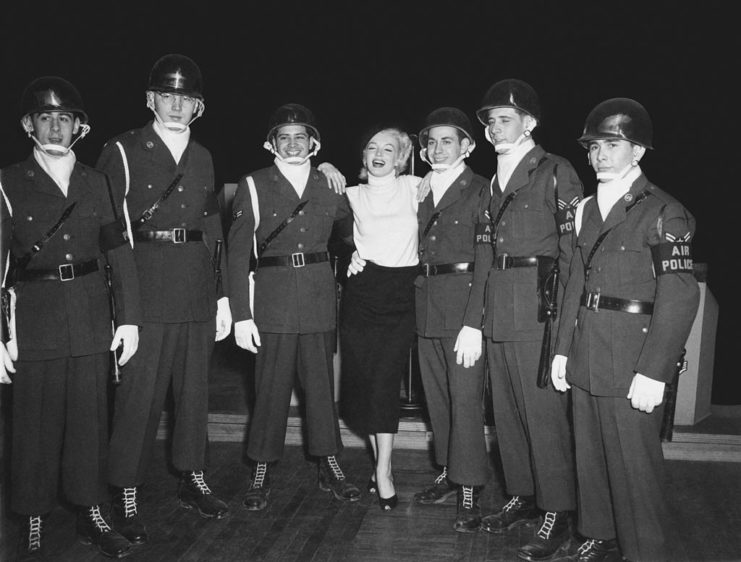Marilyn Monroe standing with six military police personnel