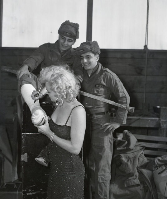 Marilyn Monroe signing Airman Third Class Gerald Kasper's leg cast while his brother watches