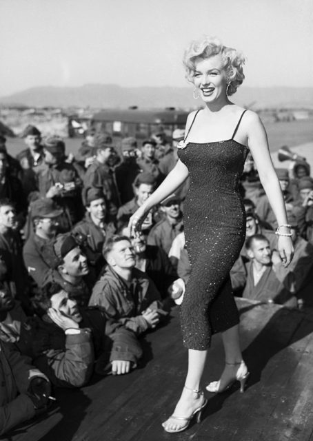 Marilyn Monroe standing onstage in front of a group of American troops