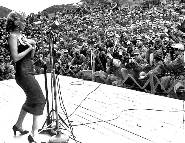 Marilyn Monroe standing onstage in front of a group of soldiers