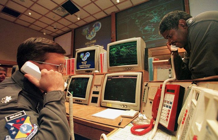 Two military commands speaking on telephones while sat around computer screens