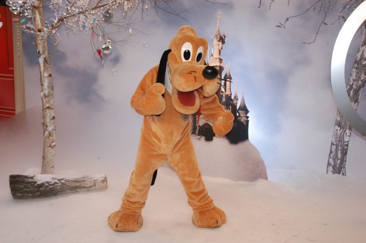 Pluto mascot holding a thumbs up while standing in a wintertime scene