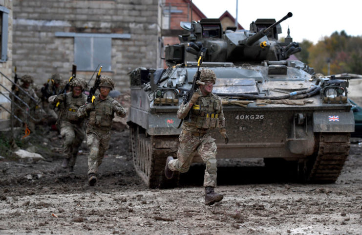 Armed soldiers running alongside a military tank