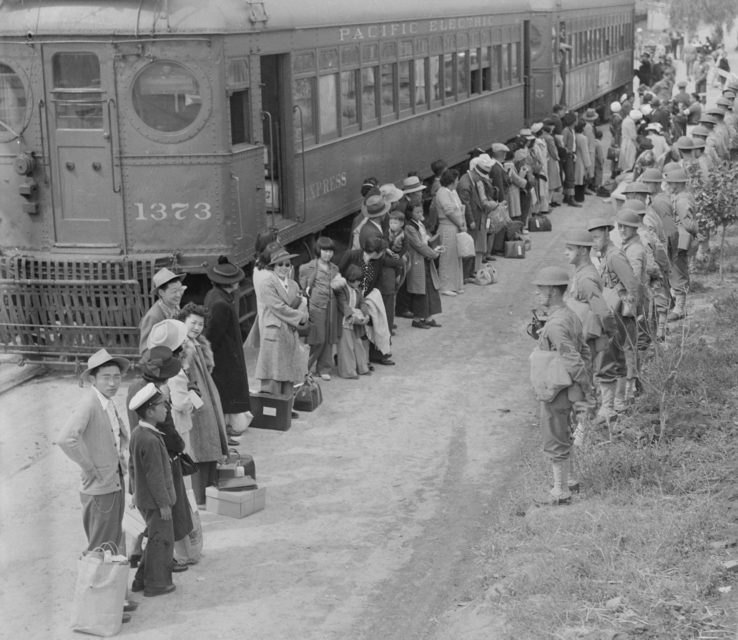 Japanese Americans getting off a train while American military personnel stand guard