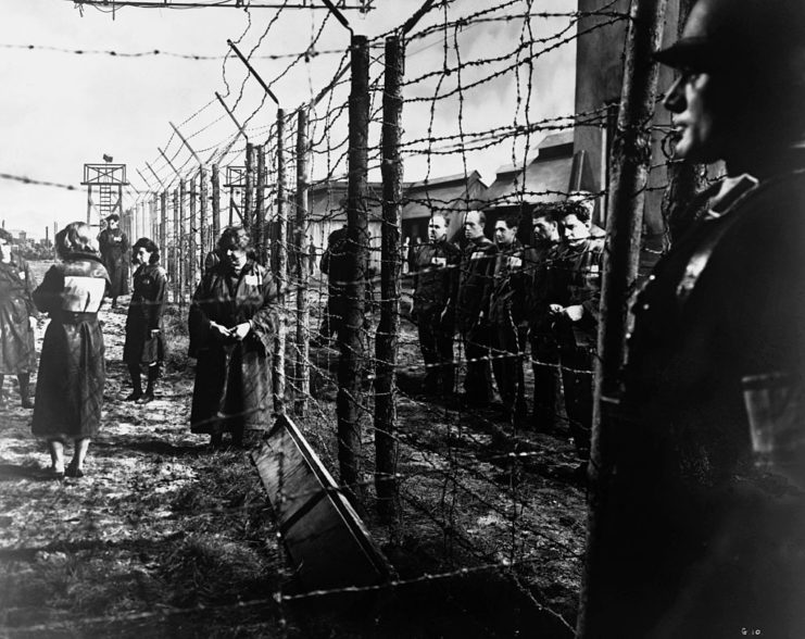 Prisoners standing on both sides of an electrified fence