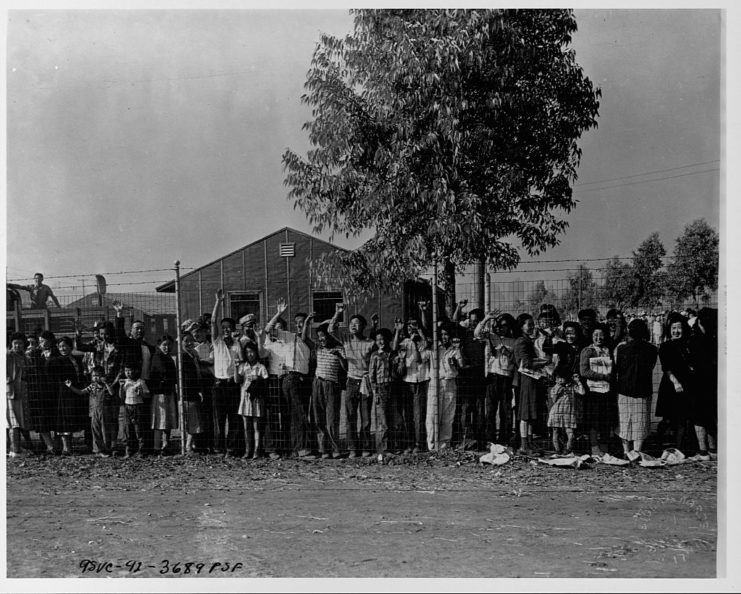 Japanese-Americans waving behind a barbed wire fence