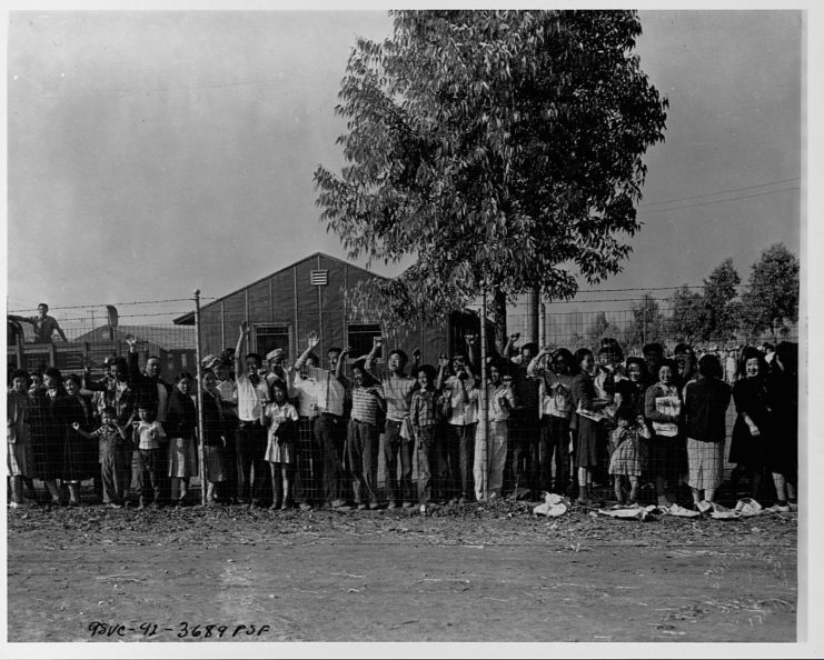 Japanese-Americans waving behind a barbed wire fence