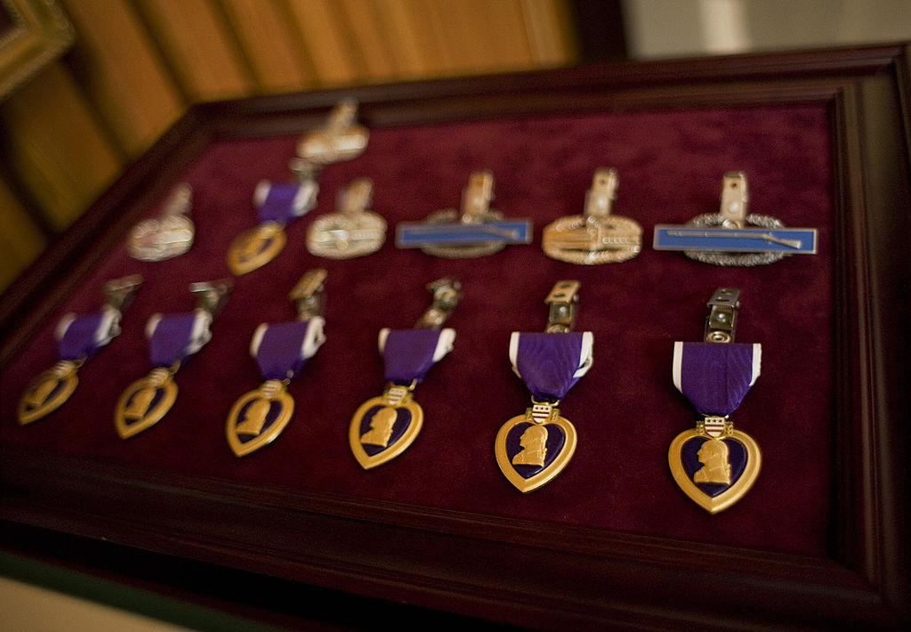 Six Purple Heart medals against a red backdrop