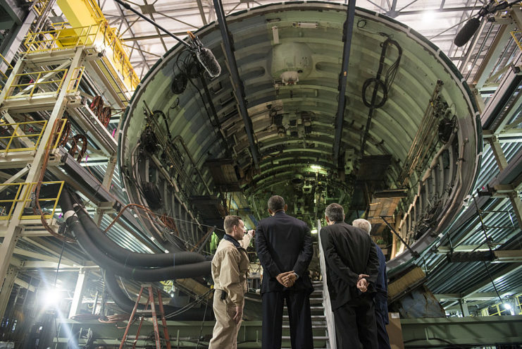 Barak Obama and others looking up at a submarine under construction