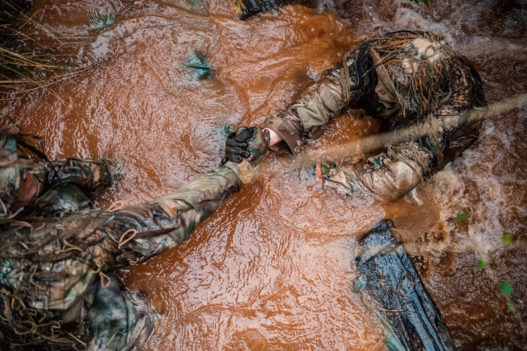 Two students at the US Army Sniper School reaching out to each other while wading through dirty water