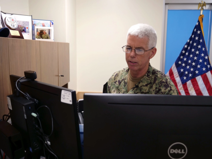 Vice Admiral Karl Thomas standing behind two computer monitors