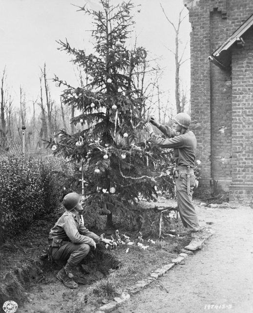 Two American soldiers decorating a Christmas tree outside