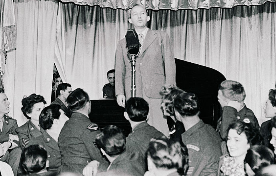 Bing Crosby performing in front of a crowd of civilians and soldiers