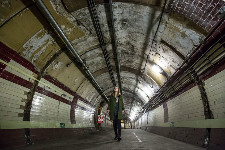 Woman walking through a large tunnel at Down Street Tube Station