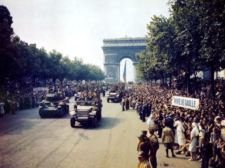 French citizens crowded along a road as cars drive by