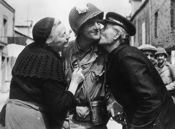 Elderly French couple kissing the cheeks of a US soldier