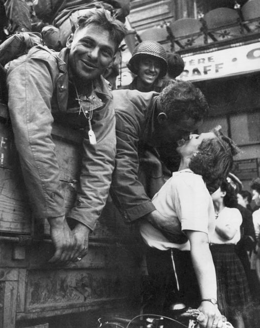 American soldier kissing a French woman while his comrades look on