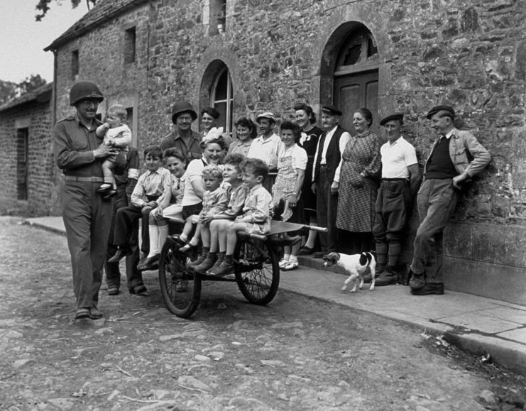 US soldiers standing with French children and adults outside of a brick building