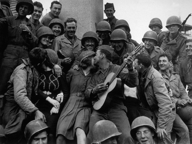 French citizens and US soldiers crowded around a GI holding a guitar