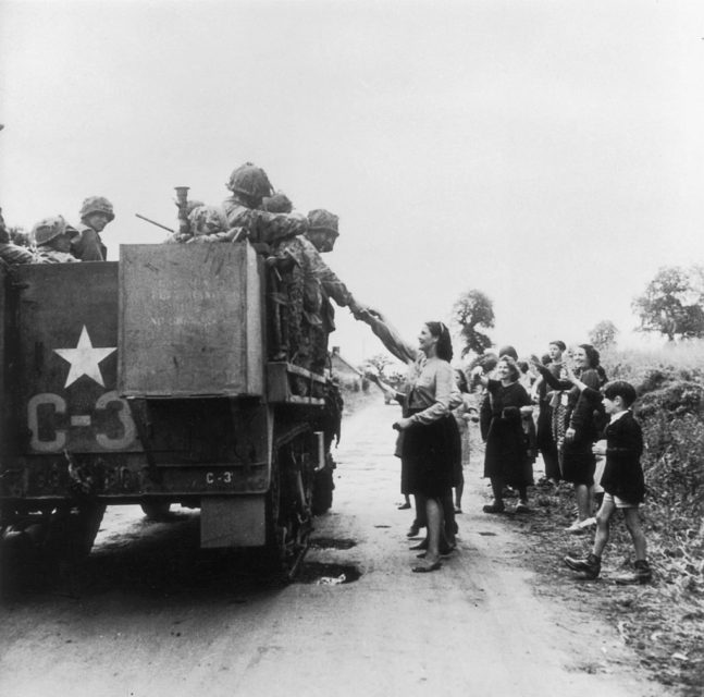 French woman reaching up to American troops sitting in a vehicle