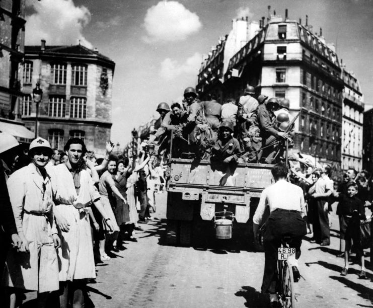 Crowds gathered along the side of a street while a car drives through