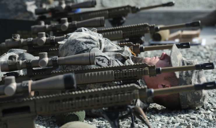 US Army Mobile Sniper School trainee lying beneath sniper rifles