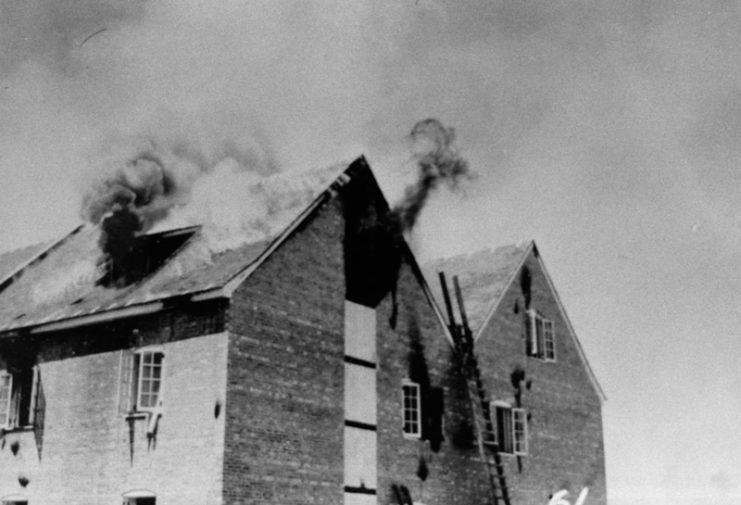 Wooden homes on fire, with smoke rising from their roofs