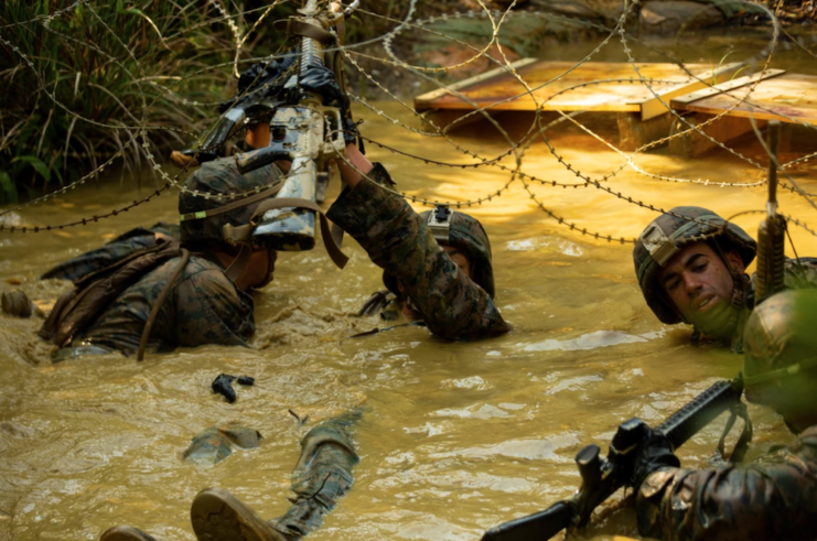 Island Warriors wading in muddy water while holding their weapons