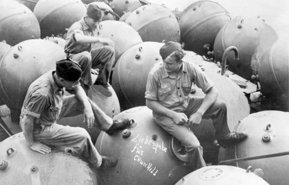 Three German soldiers sitting atop a pile of sea mines