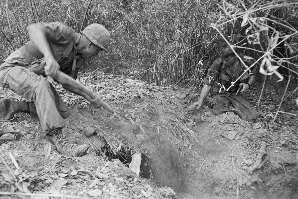 While a buddy, with pistol ready, kneels by, a G.I. of the 2nd Battalion, 18th Infantry, shovels dirt into a tunnel entrance where Viet Cong were believed to be hiding. (Photo Credit: Bettmann / Getty Images)