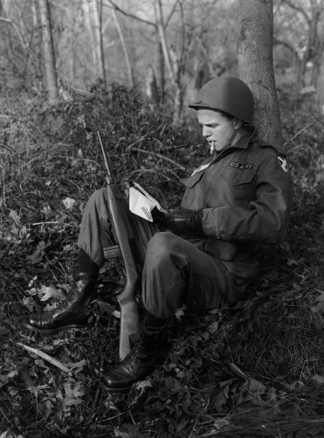 US soldier sitting against a tree while reading a letter