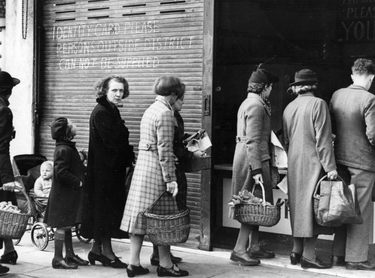 Women and children standing in line with baskets outside of a shop