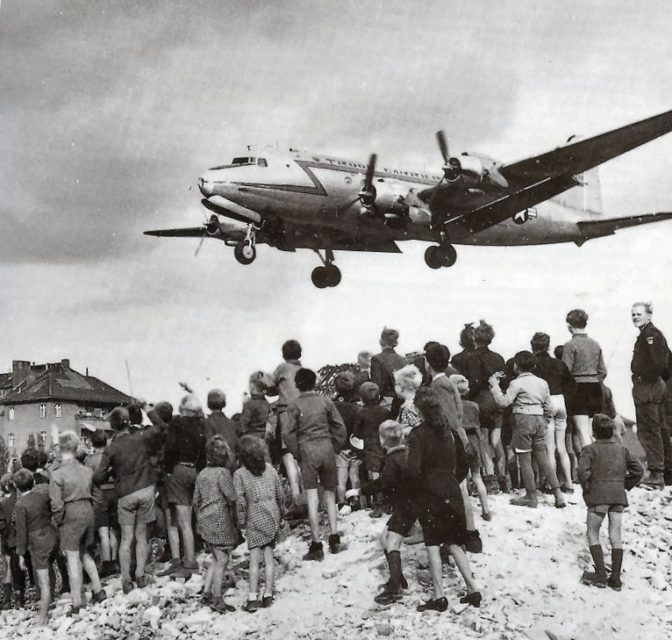 Crowd gathered beneath a landing Douglas C-54 Skymaster