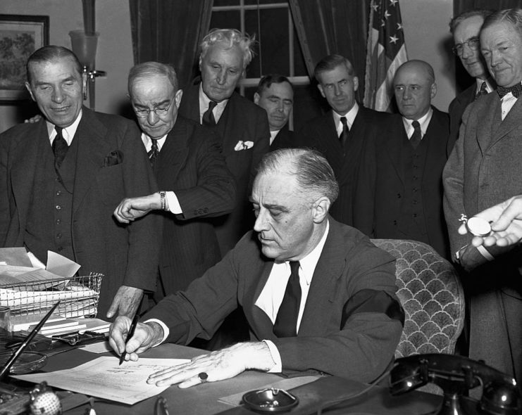 Cabinet members watching as Franklin D. Roosevelt signs a proclamation of war at his desk