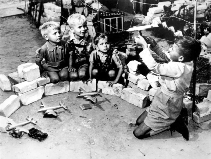 Young boys watching another child holding a toy airplane