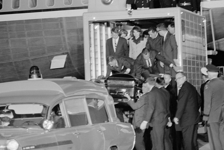 Jacqueline and Robert Kennedy watching as people lower John F. Kennedy's casket into a hearse