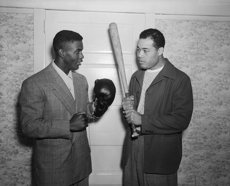 Jackie Robinson wearing a pair of boxing gloves and Joe Louis holding a baseball bat