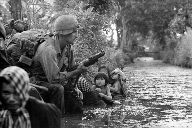 Vietnamese children looking at an American paratrooper holding an M79 grenade launcher