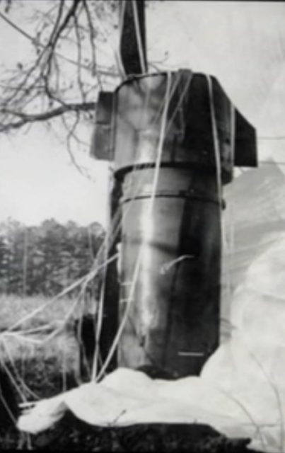 Mark 39 thermonuclear bomb sitting nose-up in the dirt, with its parachute deployed