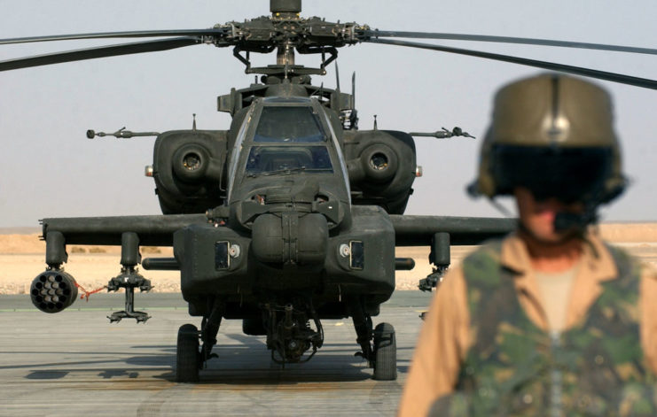 Pilot standing in front of an AH-64 Apache helicopter on the tarmac