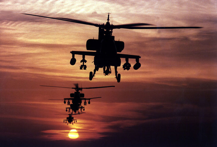 Three AH-64 Apache helicopters in flight at sunset