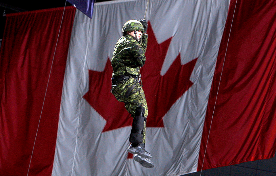 Canadian Armed Forces member hanging from a rope in front of the Canadian flag