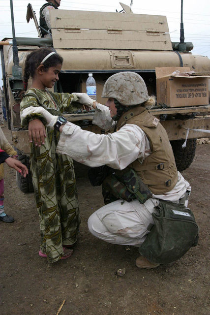 US Army motor transport operator kneeling before a young girl