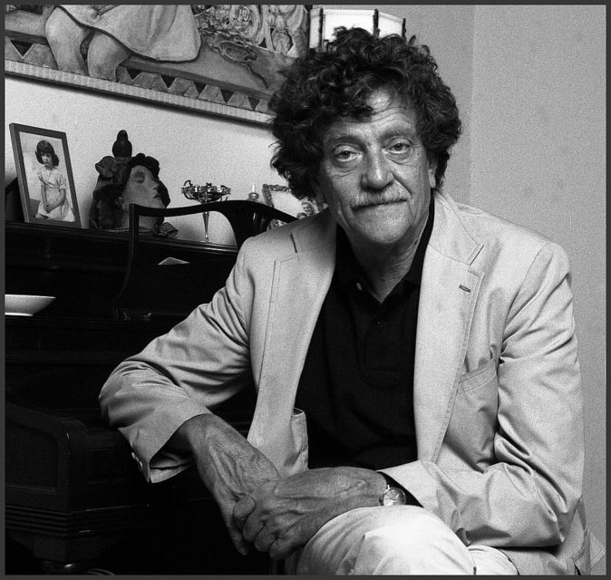 Kurt Vonnegut leaning against a piano