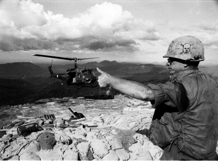 US army soldiers giving a thumbs up as a HU-1 helicopter hovers in the background. 