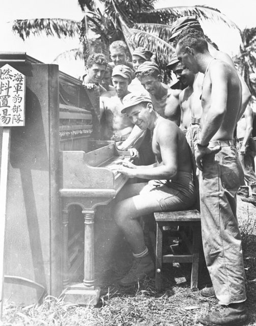 An American pack Howitzer unit listening to a corporal playing the piano